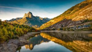 mountain with water refllection in a lake with autumn tree forest and a small town in aragon, heusca, spain